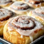 Freshly baked cinnamon rolls topped with icing on a wooden table