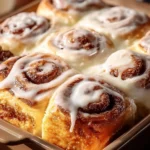 Freshly baked cinnamon rolls topped with creamy icing on a wooden table