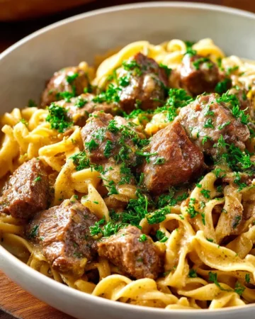 Bowl of slow cooker beef stroganoff served with noodles and garnished with parsley.