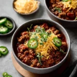 Bowl of spicy beef chili garnished with fresh cilantro and peppers