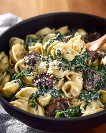 Creamy spinach mushroom tortellini garnished with herbs in a bowl