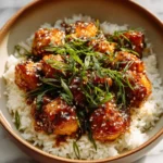 Plate of sesame chicken garnished with sesame seeds and green onions
