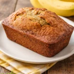 Loaf of freshly baked banana bread with sliced bananas on a wooden table