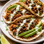 Black Bean Quinoa Tacos topped with cilantro lime cashew crema on a wooden table.
