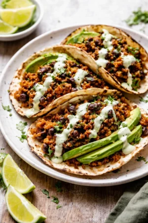 Black Bean Quinoa Tacos topped with cilantro lime cashew crema on a wooden table.