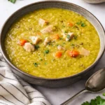 Bowl of classic split pea soup topped with fresh herbs and crusty bread.