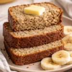 Slice of easy moist banana bread on a wooden table with bananas in the background