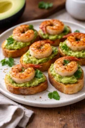 Garlic shrimp crostini topped with avocado on a platter