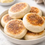 Freshly baked sourdough English muffins on a wooden cutting board.