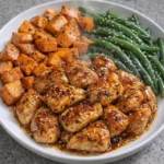 Honey garlic chicken served with roasted sweet potatoes on a dinner plate.